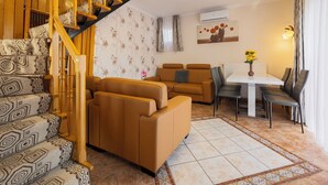Uma sala de estar com um sofá marrom, uma mesa de jantar com cadeiras, uma escada com degraus estampados e um ar condicionado fixado na parede.