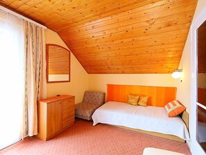 A bedroom with a sloped ceiling, a bed with orange headboard, a wooden dresser, and a patterned chair. - Flamingo by Interhome (Balatonalmadi)