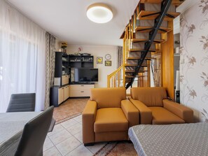 A living room with a sofa, a TV, a staircase, and a dining area.