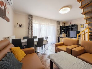 A living room with a sofa, a coffee table, a dining area with chairs, a TV, and a staircase.