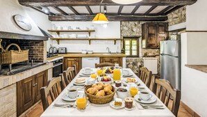Une cuisine rustique avec des poutres apparentes, un mur en pierre et une table à manger mise pour le petit-déjeuner.