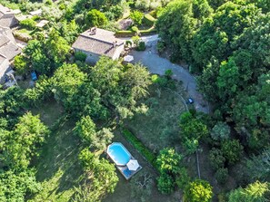 Eine Vogelperspektive zeigt eine Wohngegend mit einem Swimmingpool, umgeben von üppiger Vegetation und einem Kiesweg.