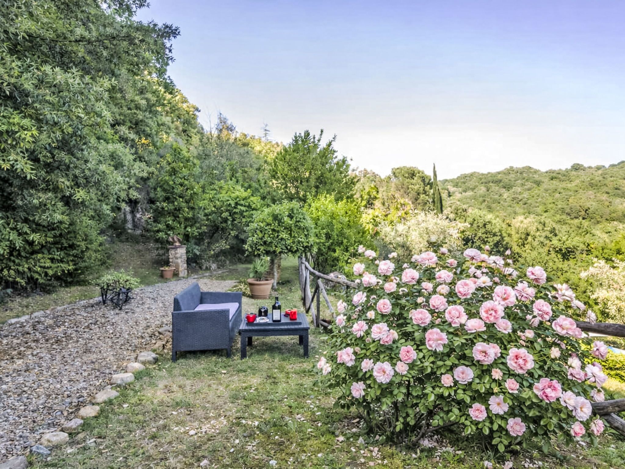 Un giardino con un'area salotto, un tavolo con delle bottiglie e un roseto.