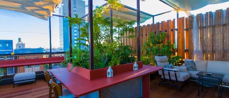 Un bar en la azotea con suelo de madera, una barra roja y zonas de estar con sofás y sillones.