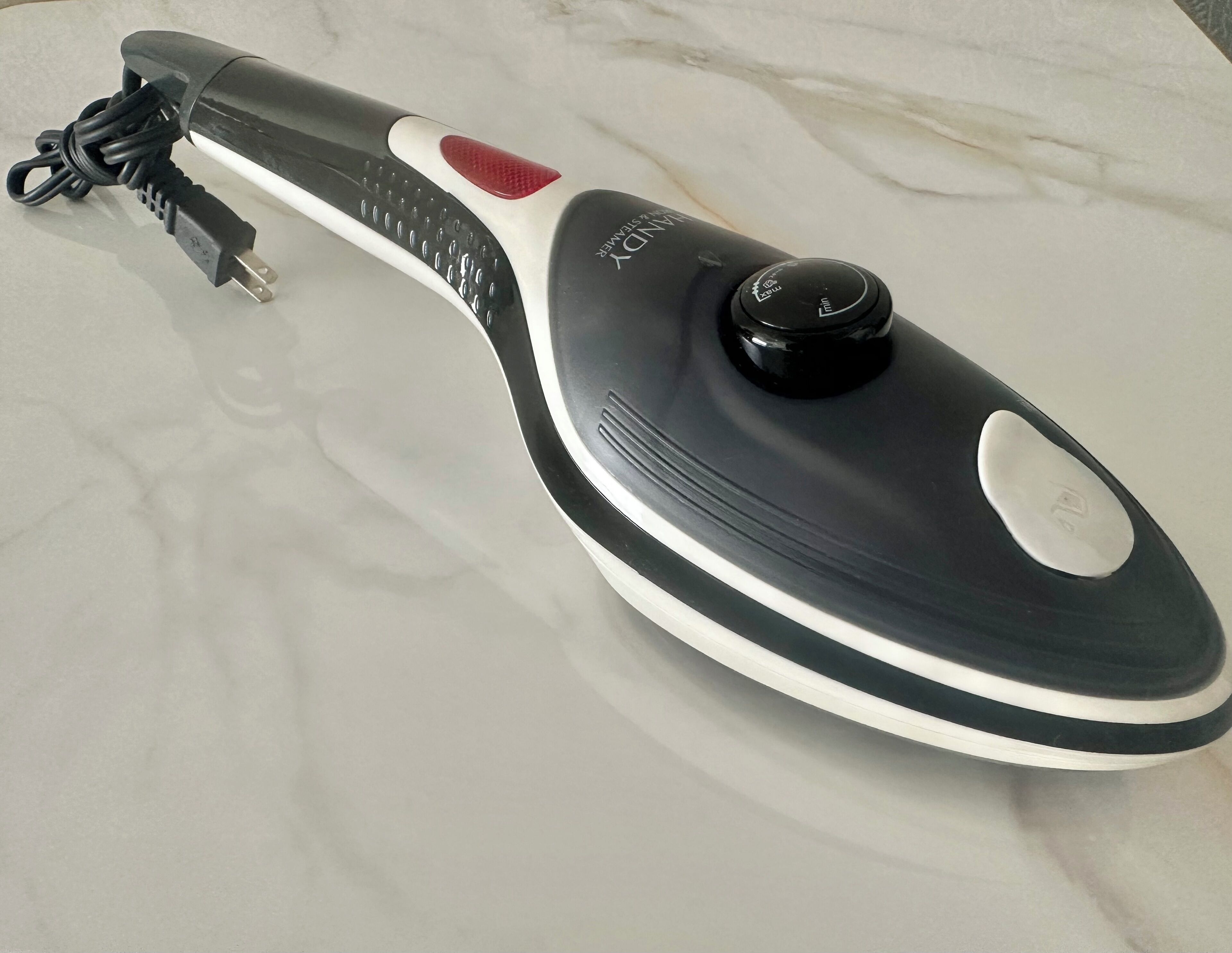 A black and white iron with a red button and a power cord.