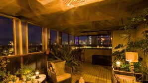 Un bar en la azotea con vistas a la ciudad, mesas al aire libre y plantas en macetas.