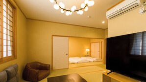 Habitación de hotel con sofá, televisión, una mesita de madera y puerta corredera que da a un dormitorio.
