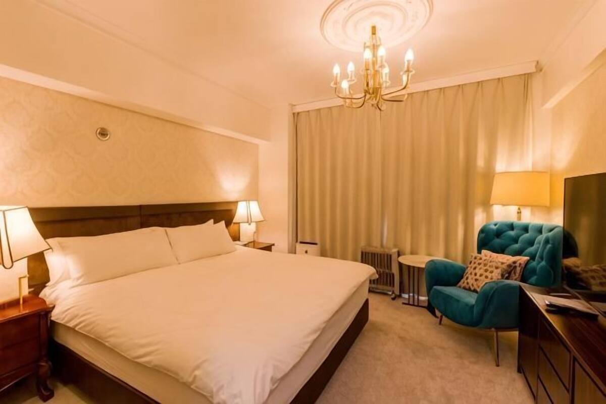 A hotel room with a large bed, a small table, a blue armchair, and a TV.