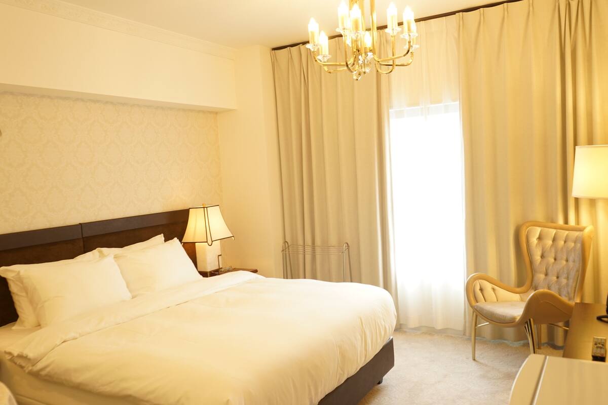 A hotel room with a large bed, a chair, a desk, and a chandelier.
