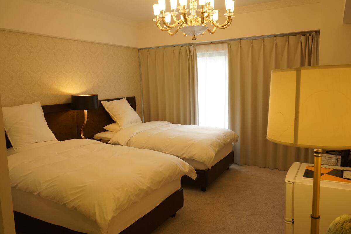 A hotel room with two beds, a chandelier, a nightstand, and a lamp.