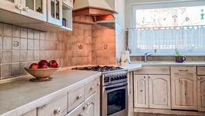 A kitchen with a gas stove, oven, wooden cabinets, and a window with a view.