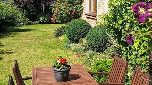 A wooden table with chairs, a potted plant, and a garden with various plants and flowers.