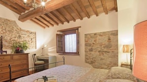 A bedroom with a bed, wooden ceiling beams, a stone wall, a window, a desk, and a dresser. - Vacation home Bruna by Interhome (Massarosa)