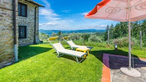 A stone building with a stone roof, a lawn with two sun loungers, and a large umbrella. - Certina 3 by Interhome (Pontassieve)