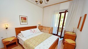 Une chambre à coucher avec un lit en bois, deux tables de chevet, une commode, une fenêtre avec des rideaux, une lampe fixée au mur et un tableau encadré.