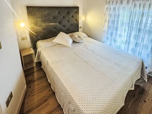 Een keurig opgemaakt bed met een beddekleed met dessin, een gestoffeerd hoofdbord en een nachtkastje met een lamp.