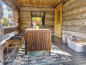 A log cabin with a wooden bench, a table, and a window with a view of trees.