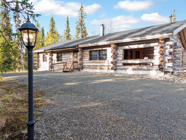 A log cabin with a gravel driveway and a lamp post.