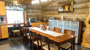 Ein rustikales Holzblockhaus-Interieur mit einem Holzesstisch, Stühlen, einer Küchenzeile mit einer Mikrowelle und einem Schrank.