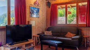 Een knus houten interieur met een leren bank, een flatscreen televisie op een houten standaard en rode gordijnen.