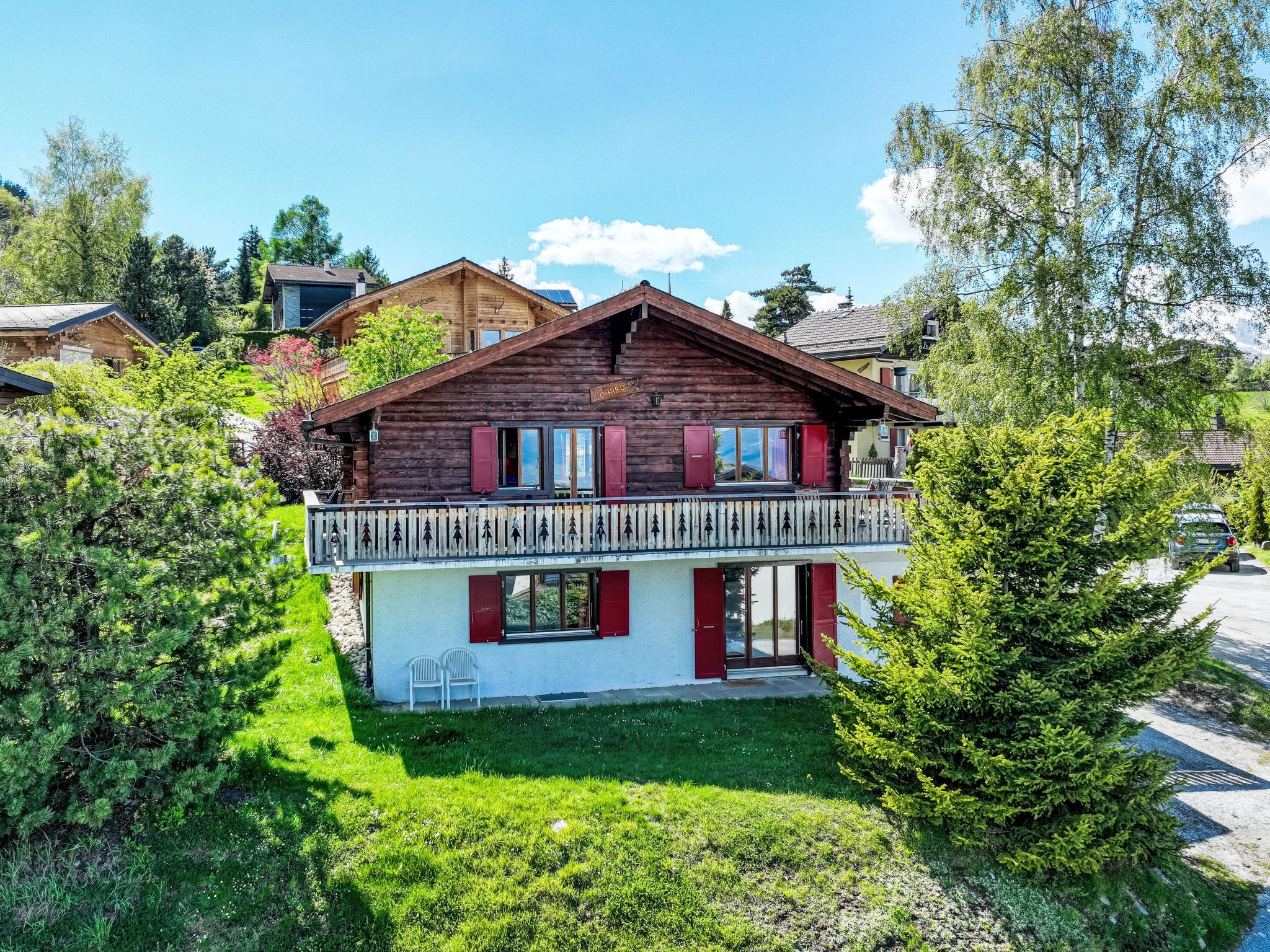 Un chalet en bois à deux étages, doté d’un balcon et entouré d’une végétation luxuriante.