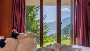 Een slaapkamer met een bed, een raam met gordijnen en twee pluchen dieren.