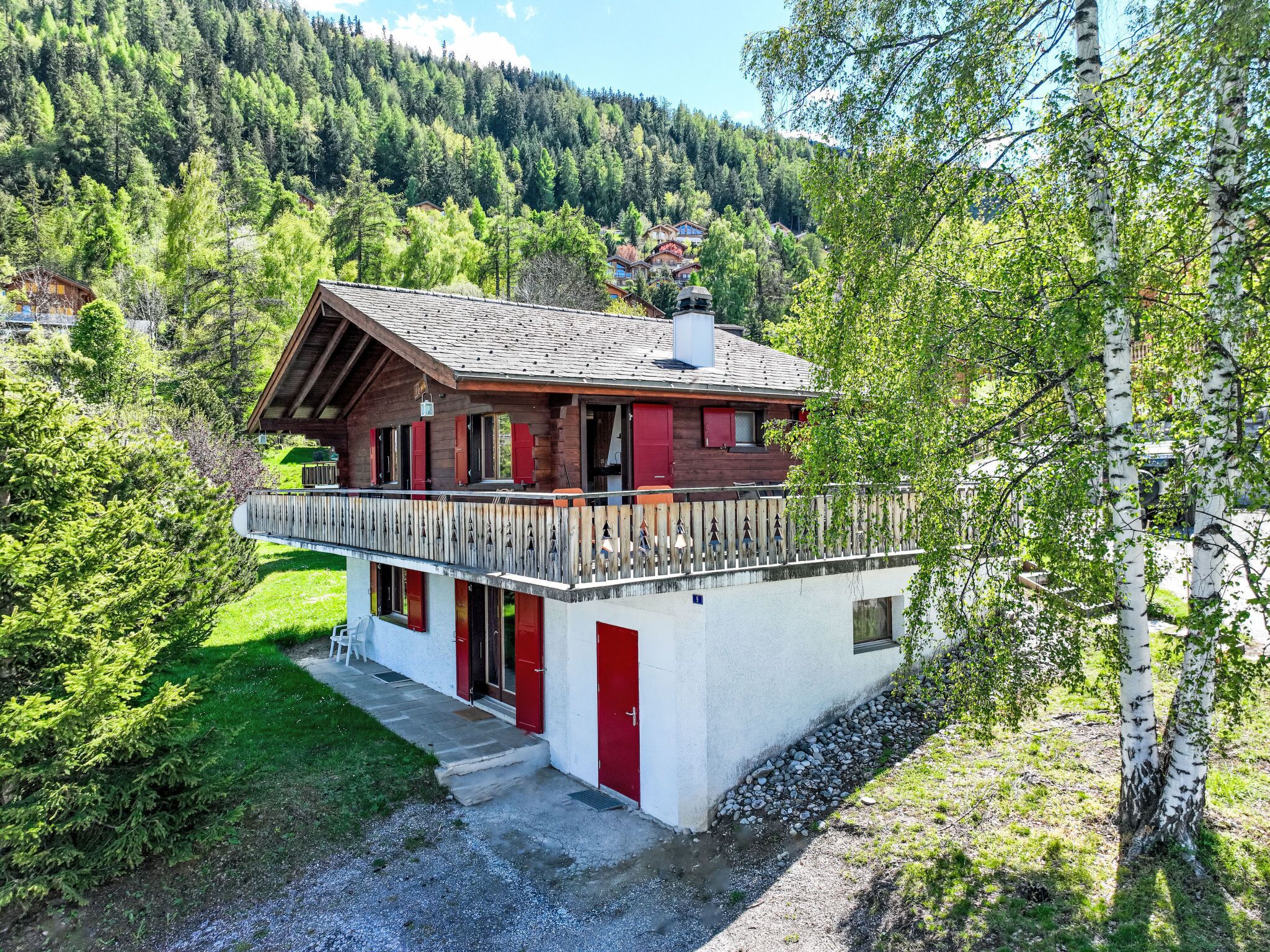 A chalet with a balcony, surrounded by forest and mountains.