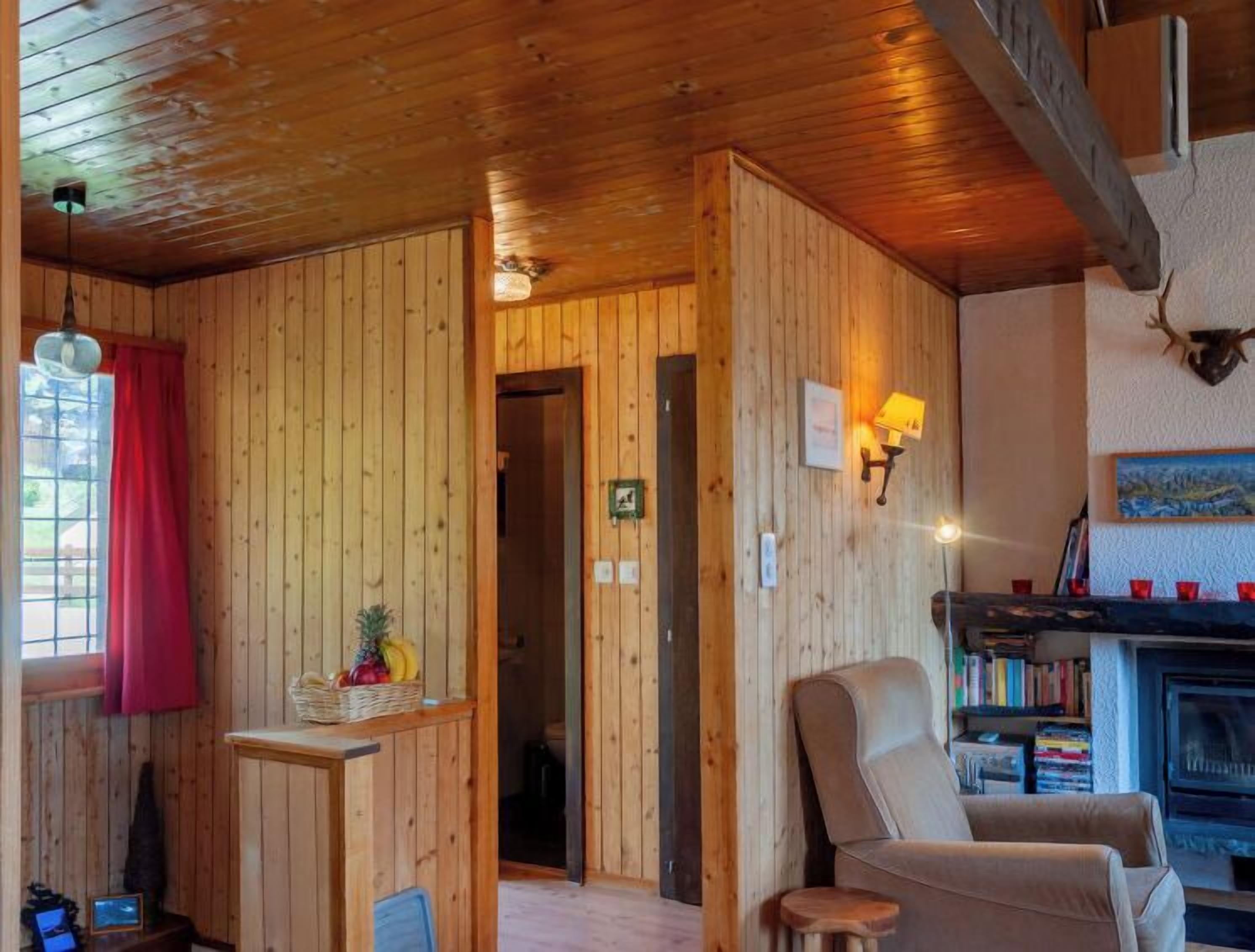 A cozy wooden cabin interior with a dining area, a living room with a fireplace, and a bookshelf.