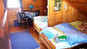 Um quarto de sótão acolhedor com teto inclinado de madeira, uma escrivaninha com cadeira e uma cama com manta colorida e um bicho de pelúcia.