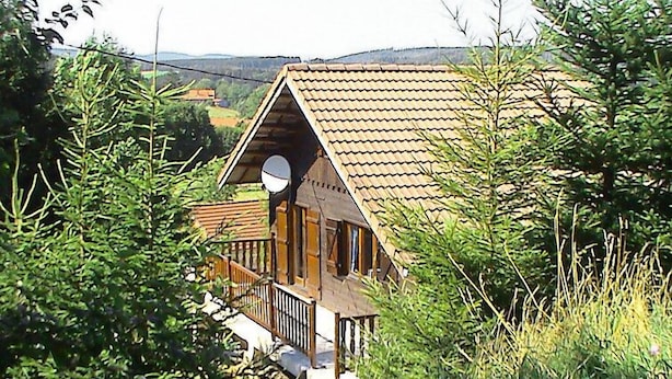 Uma cabana de madeira com telhado inclinado, varanda e antenas parabólicas.
