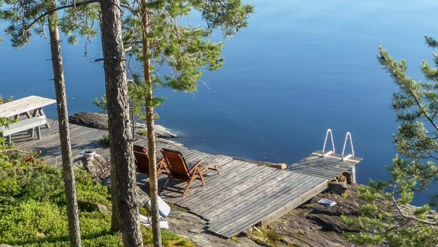 A wooden deck with two chairs and a small table, overlooking a body of water. - Keskikallio, nuasjärvi by Interhome (Sotkamo)
