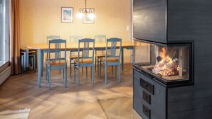 A dining area with a wooden table and chairs, a fireplace, and a hanging light fixture. - Keskikallio, nuasjärvi by Interhome (Sotkamo)