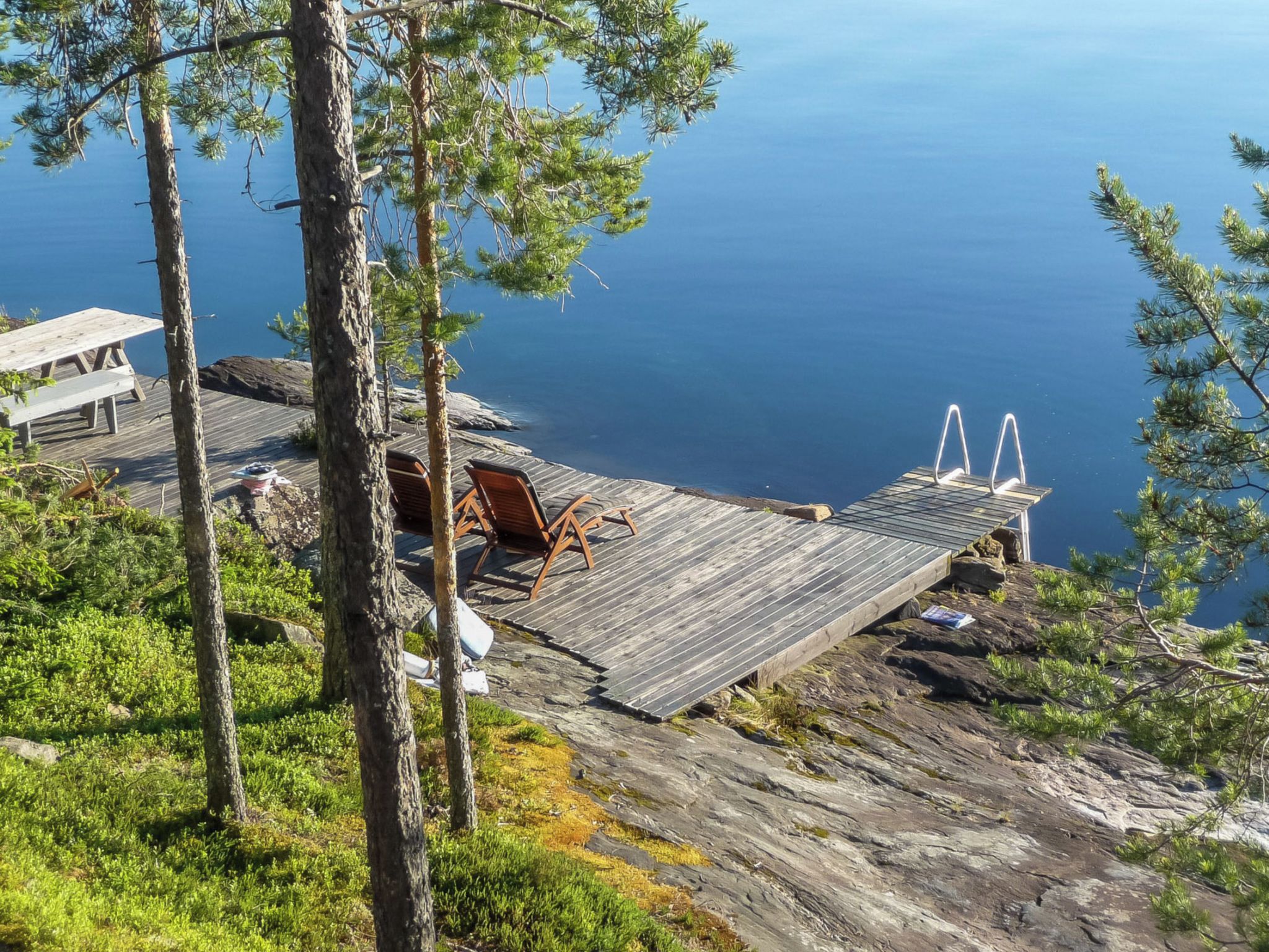 A wooden deck with a bench and a small table, overlooking a body of water.