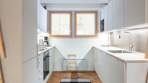 A compact kitchen with white cabinets, a built-in oven, a coffee maker, and a small ladder. - Keskikallio, nuasjärvi by Interhome (Sotkamo)