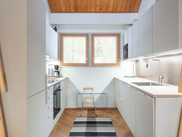 A compact kitchen with white cabinets, a built-in oven, a coffee maker, and a small ladder.