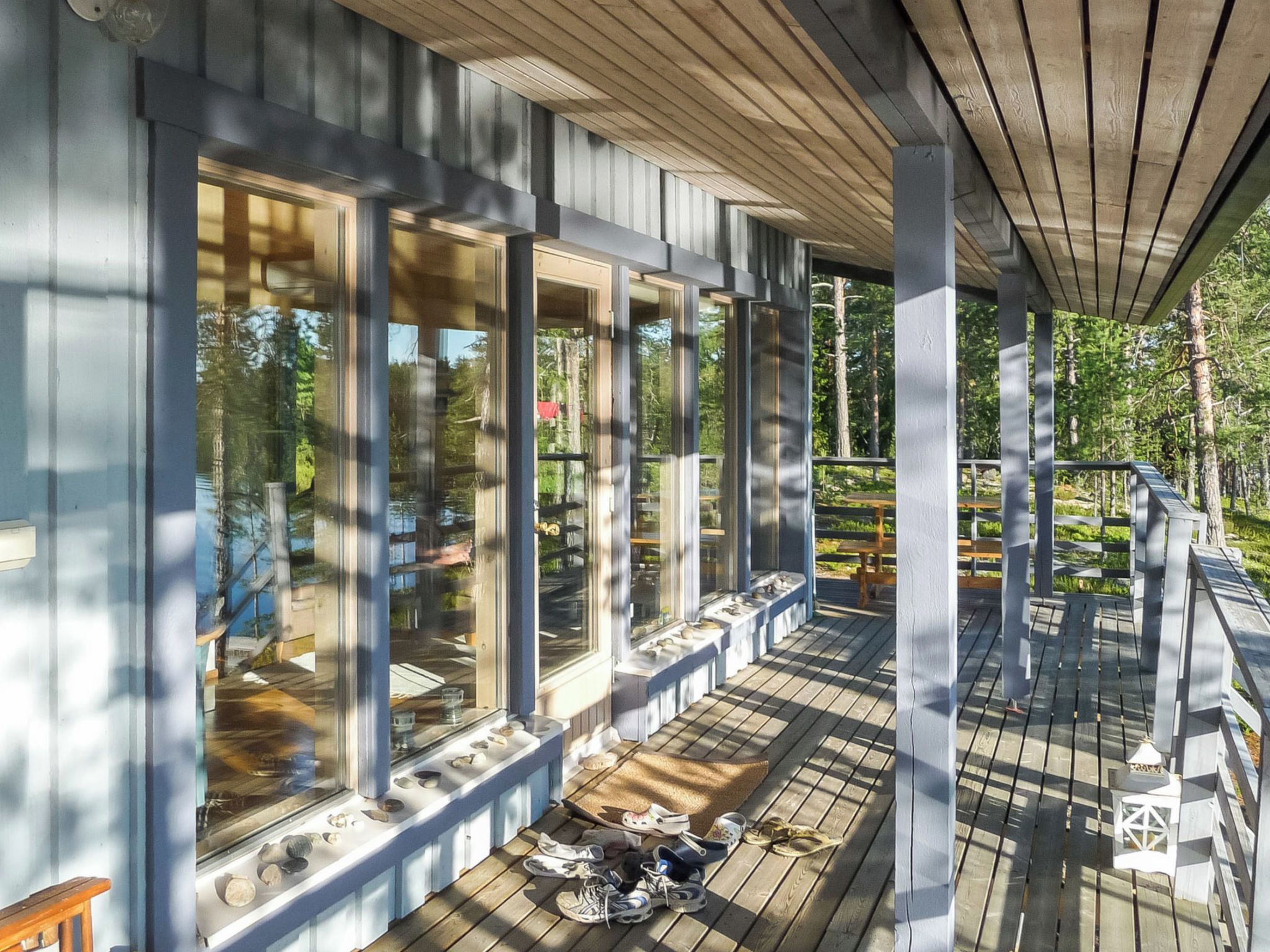 A covered wooden deck with large windows and a railing.