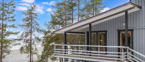 Moderni mökki, jossa on parveke, jolta avautuu näkymä lumiseen maisemaan ja vesistöön.