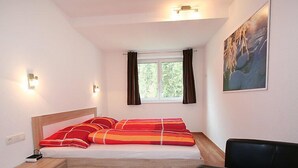 A bedroom with a bed, a nightstand, a chair, a window with curtains, and a painting on the wall. - Collina by Interhome (See)