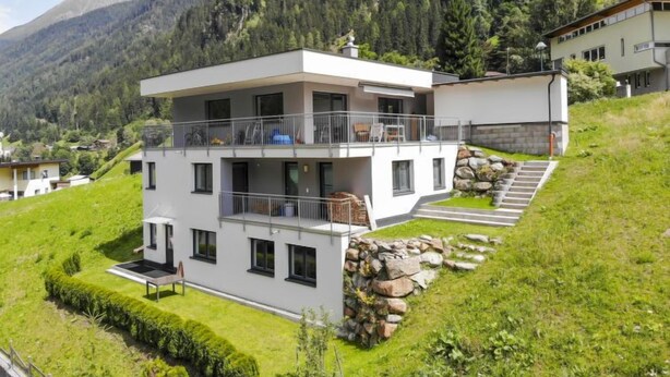 A modern two-story house with a balcony, surrounded by lush greenery and mountains. - Collina by Interhome (See)