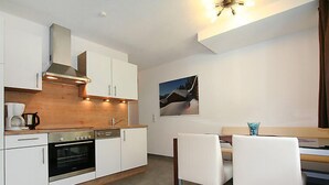 A modern kitchen with white cabinets, a built-in oven, and a wooden countertop. There is a dining area with a table and chairs, and a painting on the wall. - Collina by Interhome (See)