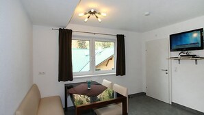 A modern living room with a sofa, dining table, and a flat-screen TV mounted on the wall. - Collina by Interhome (See)