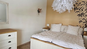 Un dormitorio con cama, cómoda, mesita de noche, lámpara de pared y una planta decorativa.