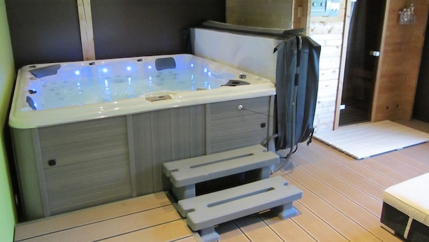 Una bañera de hidromasaje con escalones que la conducen, un banco de madera y una puerta al fondo.