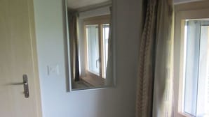 Una habitación con una banca empotrada, un espejo, un radiador y una ventana con cortinas.