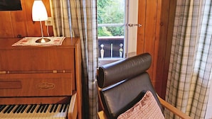 Una habitación de madera con un piano, una silla, una lámpara y cortinas.