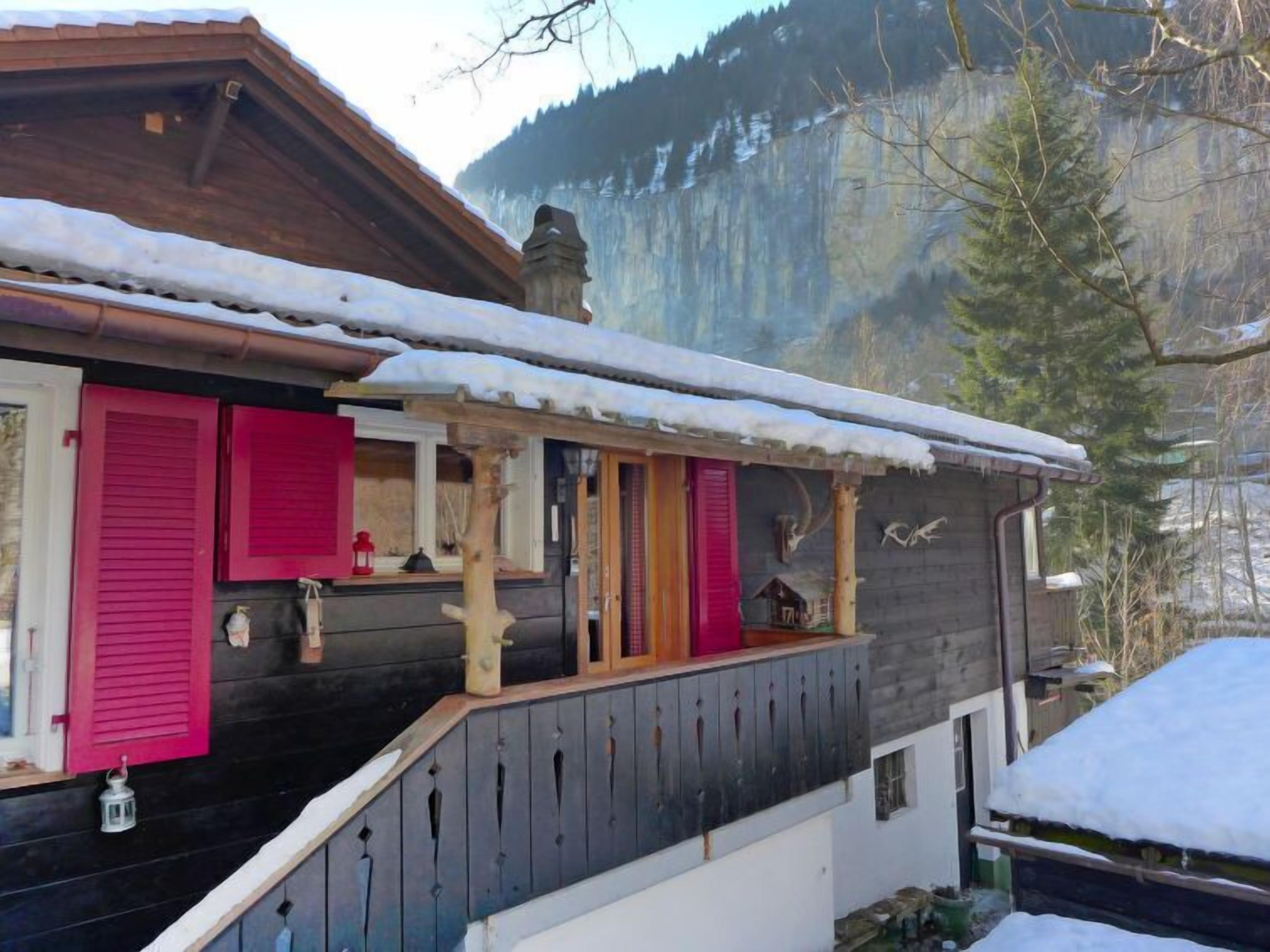 Ein Holzhaus mit rosafarbenen Fensterläden, einem Balkon und einem verschneiten Berggrund.
