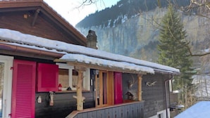 Una casa de madera con contraventanas rosadas, un balcón y una montaña nevada al fondo.
