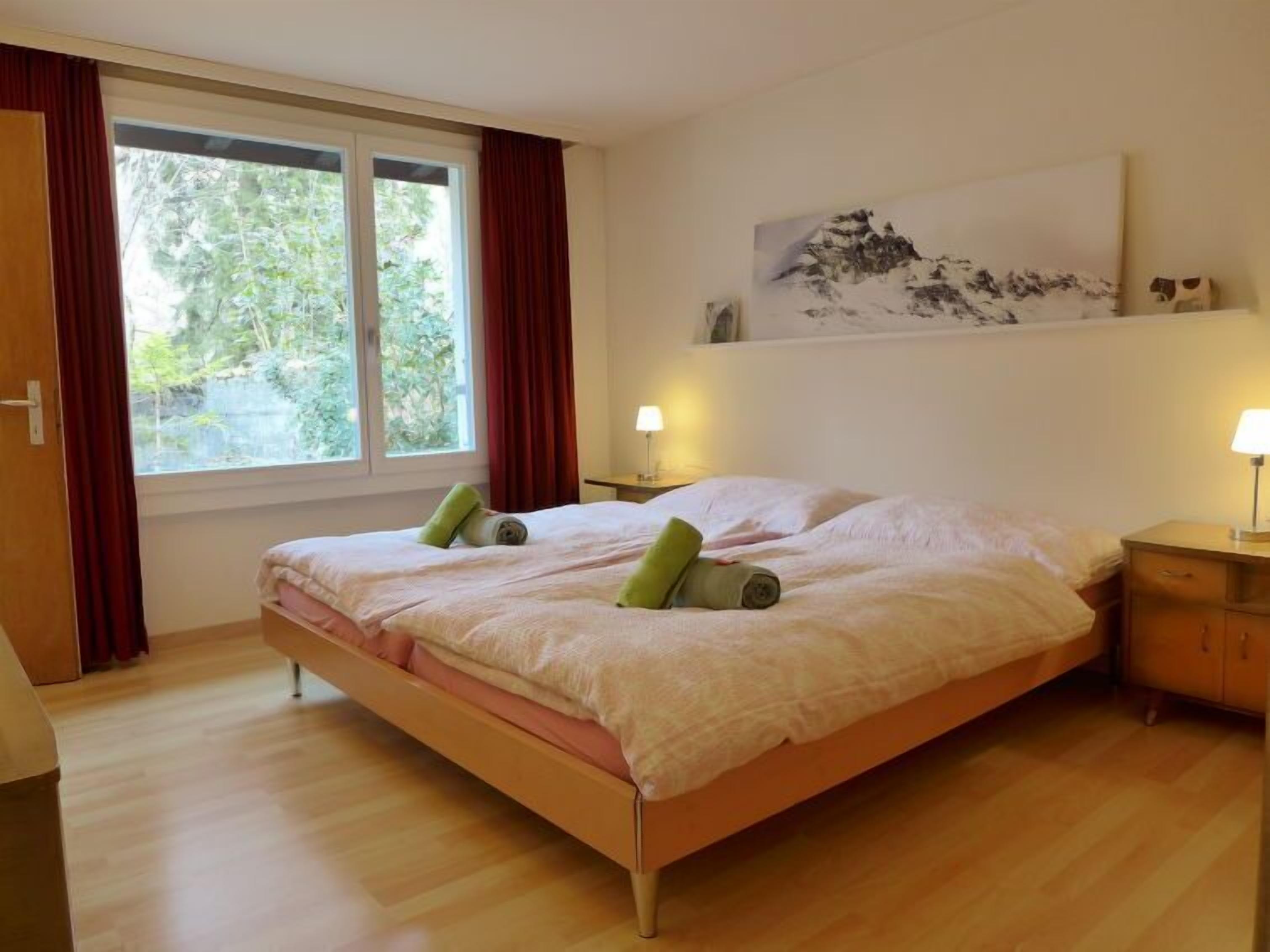 Ein Schlafzimmer mit einem Bett, zwei Nachttischen, einem Fenster mit Vorhängen und einem Bild an der Wand.