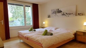 Un dormitorio con una cama, dos mesitas de noche, una ventana con cortinas y un cuadro en la pared.