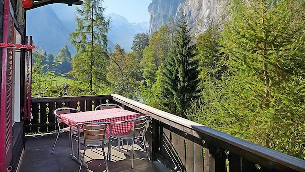 Un balcón con una mesa y sillas, con vistas a un paisaje montañoso con árboles y un acantilado.